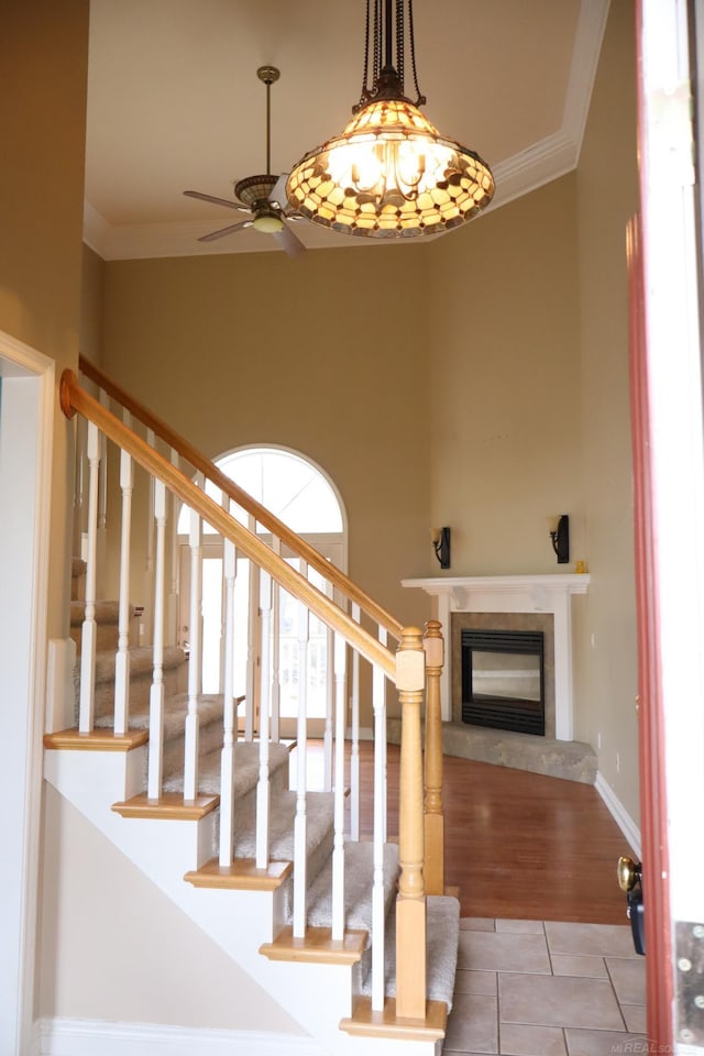 stairway with baseboards, a ceiling fan, a tiled fireplace, ornamental molding, and tile patterned flooring