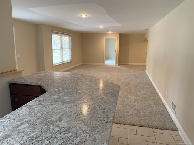 spare room featuring light carpet, baseboards, visible vents, and arched walkways