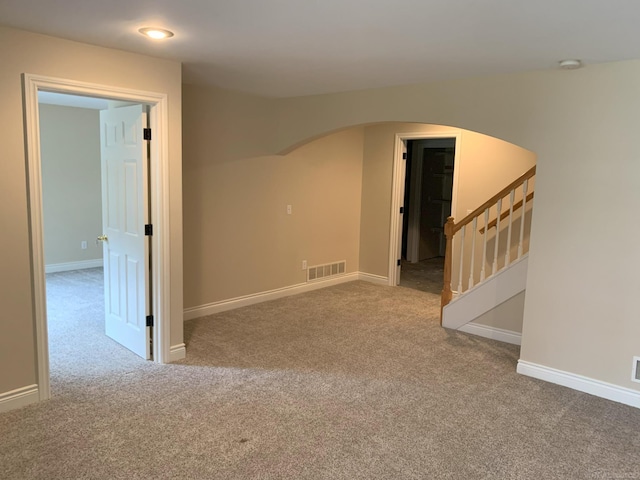 carpeted empty room with arched walkways, stairs, visible vents, and baseboards