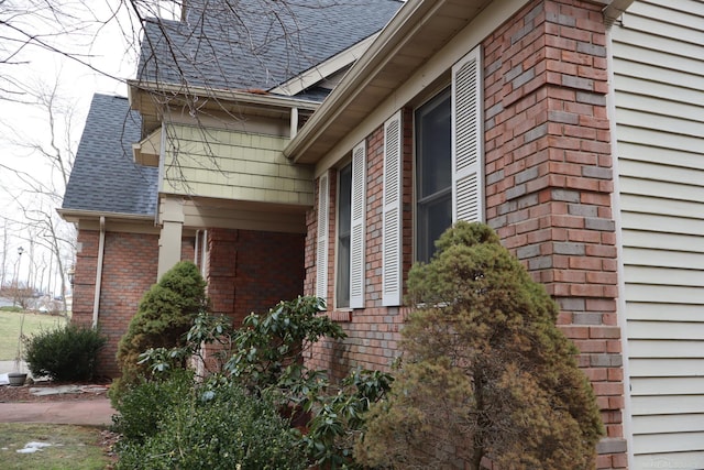 view of side of property featuring a shingled roof and brick siding