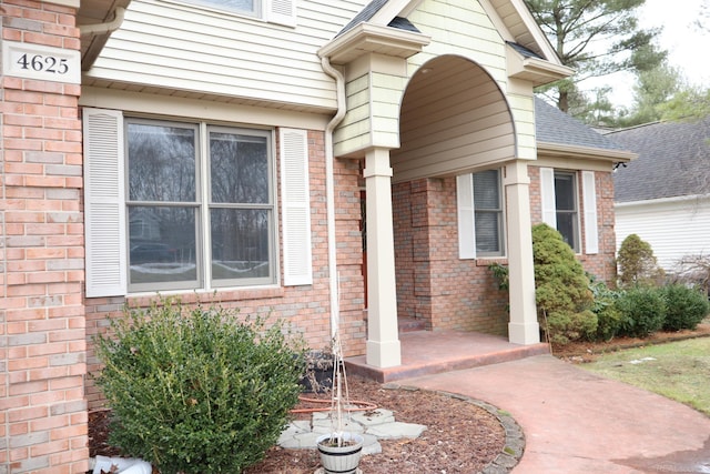 property entrance with roof with shingles and brick siding