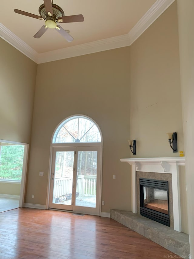 unfurnished living room with ornamental molding, a tile fireplace, a towering ceiling, and wood finished floors