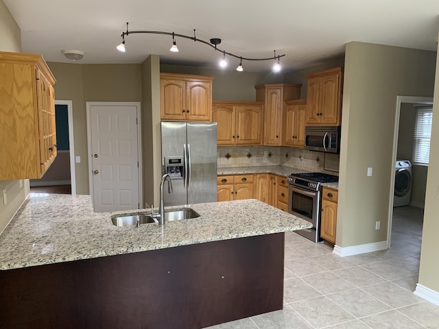 kitchen with light stone counters, washer / clothes dryer, a peninsula, stainless steel appliances, and a sink