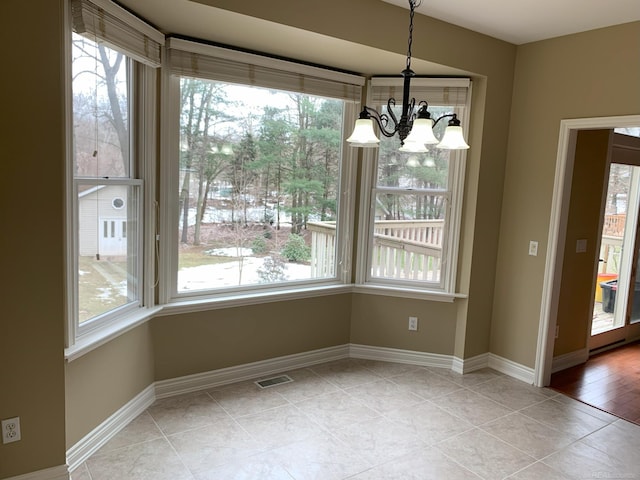 unfurnished dining area featuring visible vents, baseboards, a wealth of natural light, and an inviting chandelier