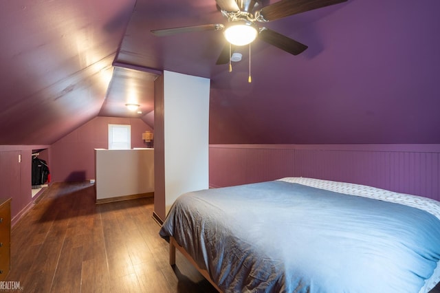 bedroom featuring a wainscoted wall, lofted ceiling, hardwood / wood-style flooring, and a ceiling fan