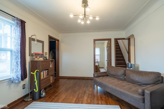 living area featuring an inviting chandelier, baseboards, arched walkways, and wood finished floors