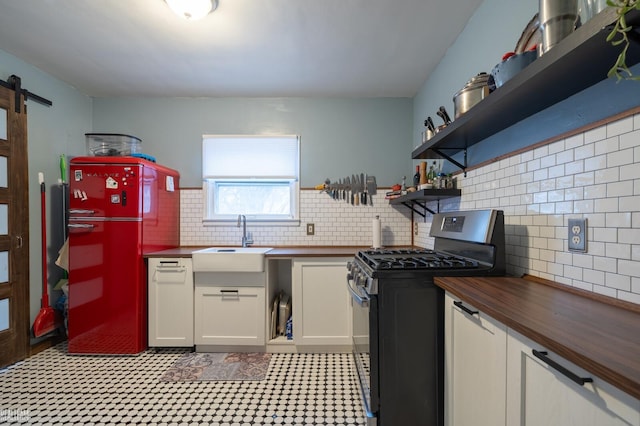 kitchen featuring freestanding refrigerator, a sink, butcher block countertops, dishwasher, and stainless steel gas range oven