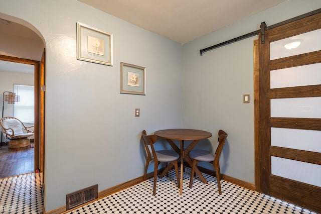 dining area with arched walkways, a barn door, visible vents, and baseboards