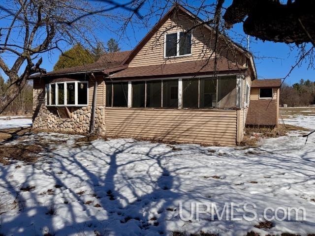 snow covered back of property with a sunroom