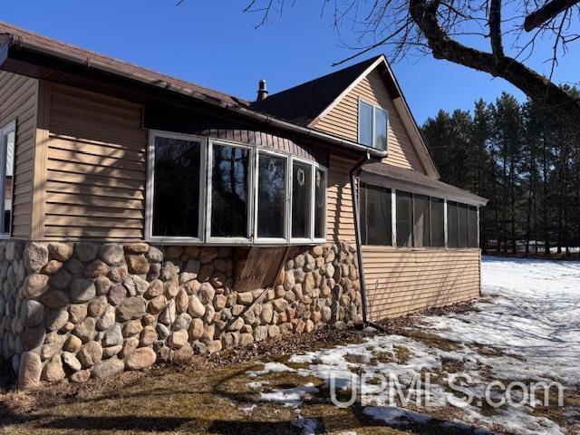 view of snow covered exterior with stone siding and a sunroom