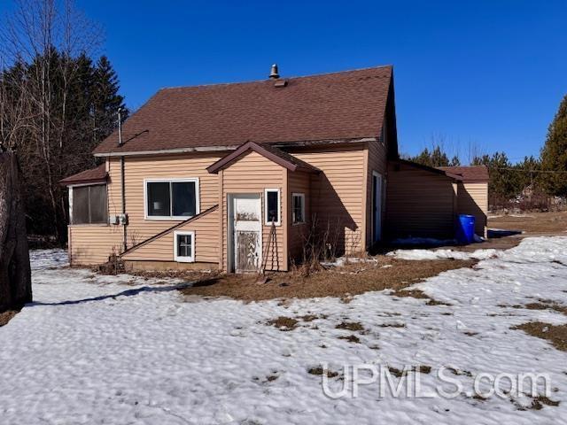 snow covered rear of property with roof with shingles