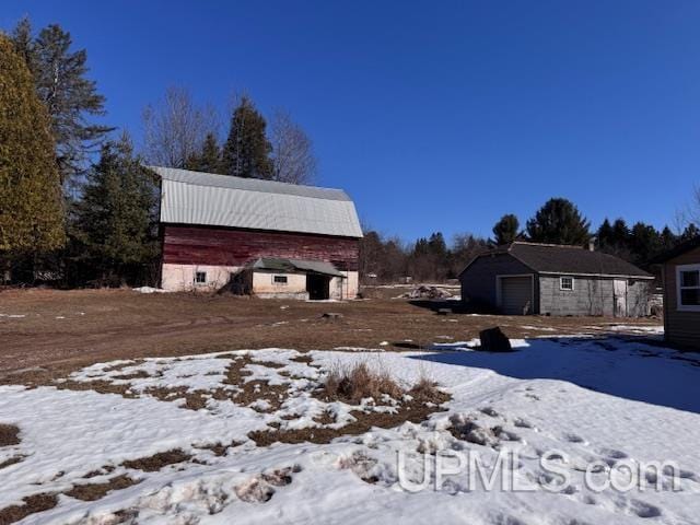 snowy yard featuring a garage, an outdoor structure, and a barn