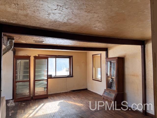 empty room featuring wood-type flooring and beamed ceiling