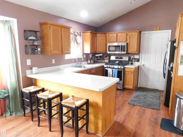 kitchen with stainless steel appliances, a peninsula, a sink, vaulted ceiling, and light countertops