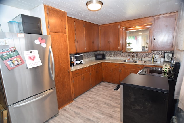 kitchen with a sink, light wood-type flooring, brown cabinets, freestanding refrigerator, and decorative backsplash