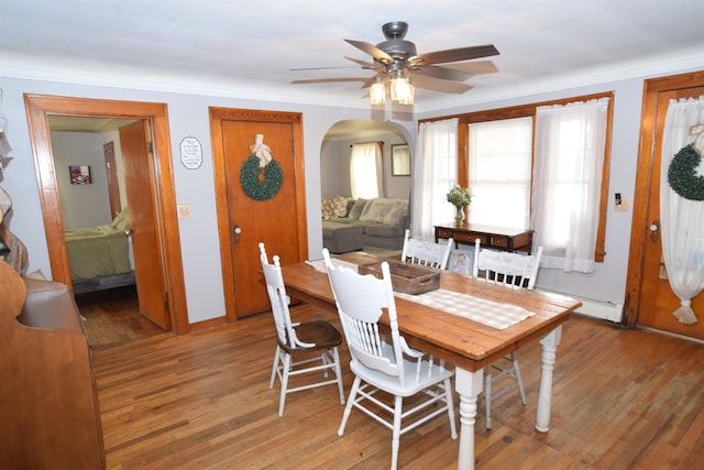 dining area with light wood-style flooring, arched walkways, a ceiling fan, and ornamental molding