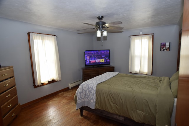 bedroom featuring multiple windows, baseboards, baseboard heating, and wood finished floors