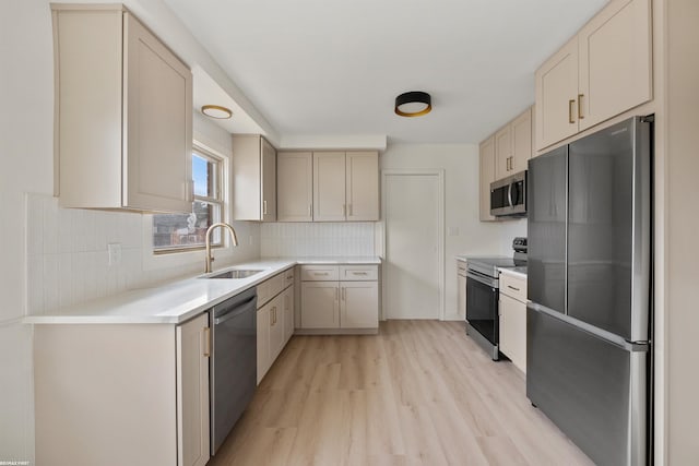 kitchen featuring stainless steel appliances, tasteful backsplash, light countertops, light wood-style flooring, and a sink