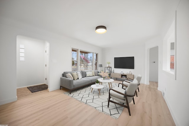 living room with light wood-style floors, baseboards, and arched walkways