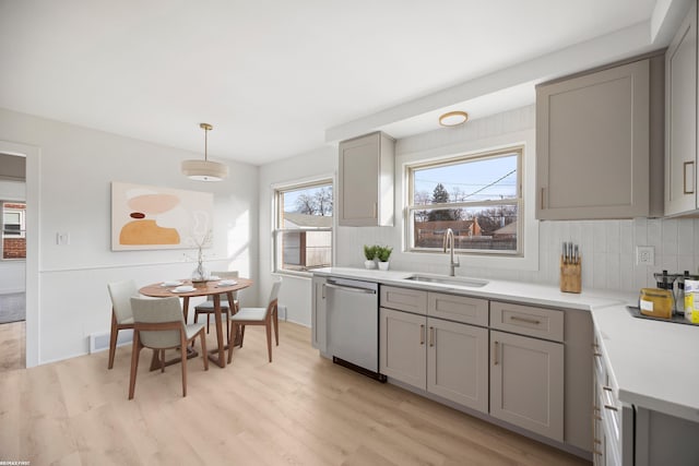 kitchen with gray cabinetry, a sink, light countertops, dishwasher, and tasteful backsplash