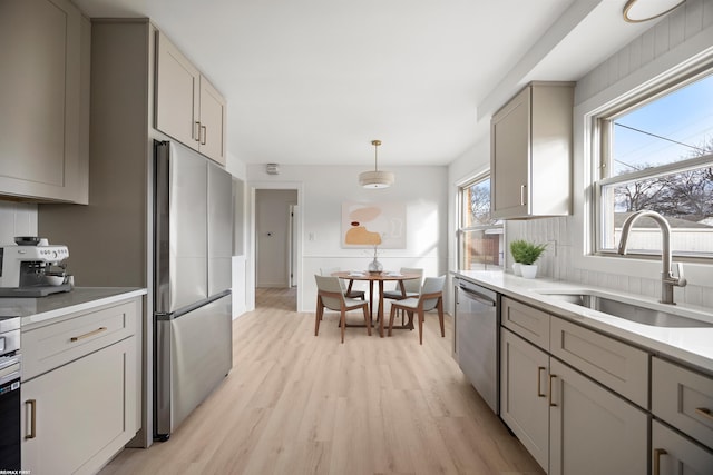 kitchen with appliances with stainless steel finishes, light wood-type flooring, light countertops, and a sink