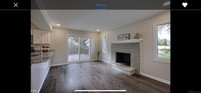 living room featuring plenty of natural light, a fireplace, baseboards, and dark wood-type flooring