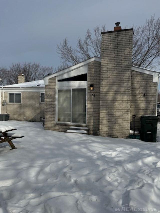 snow covered property featuring a chimney and brick siding