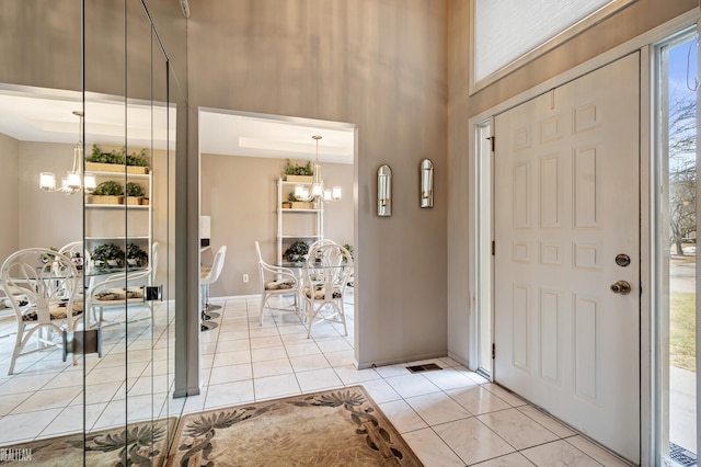 entrance foyer featuring light tile patterned floors, baseboards, a towering ceiling, and an inviting chandelier