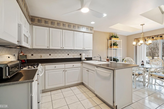 kitchen featuring dark countertops, white cabinetry, a sink, white appliances, and a peninsula