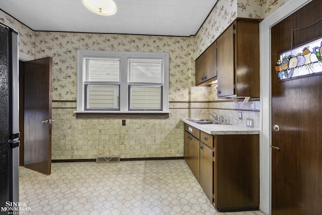 kitchen with wallpapered walls, light countertops, a sink, and a wainscoted wall