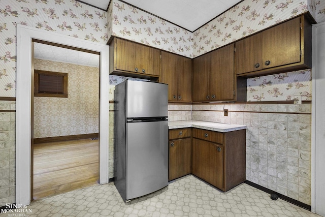 kitchen with light floors, light countertops, freestanding refrigerator, baseboards, and wallpapered walls