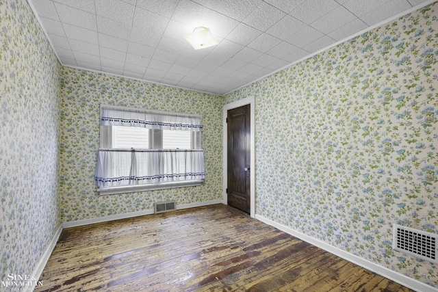 unfurnished room with wallpapered walls, baseboards, visible vents, and hardwood / wood-style floors