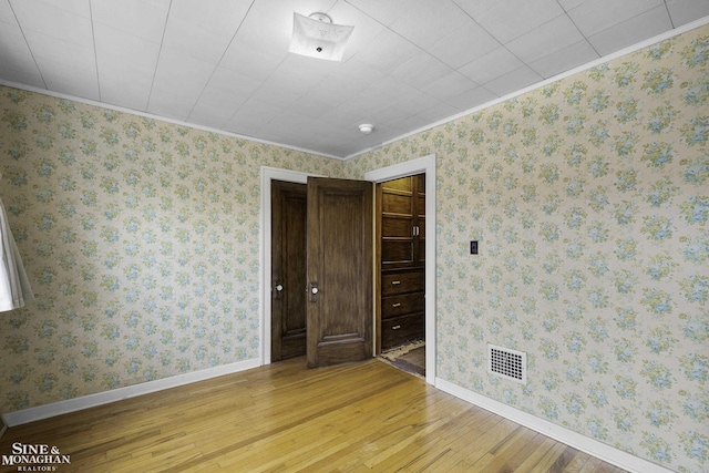 empty room featuring light wood-type flooring, wallpapered walls, and visible vents