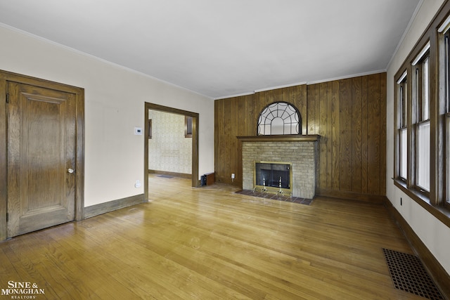 unfurnished living room featuring visible vents, a healthy amount of sunlight, ornamental molding, a brick fireplace, and light wood finished floors