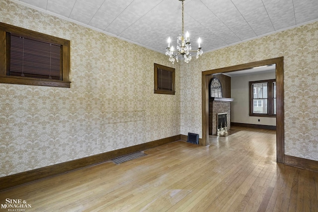 interior space featuring visible vents, light wood-style flooring, a brick fireplace, baseboards, and wallpapered walls