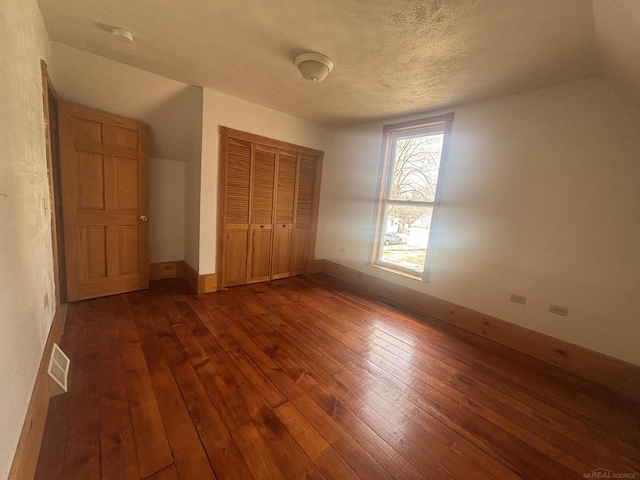 unfurnished bedroom featuring dark wood-style floors, a closet, a textured ceiling, and baseboards