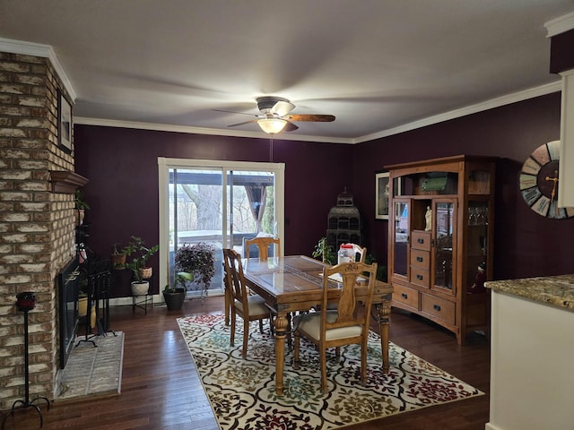 dining room featuring ceiling fan, a fireplace, dark wood finished floors, and crown molding