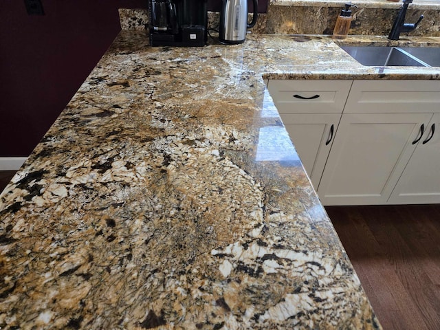 room details with dark wood-style floors, a sink, light stone countertops, and white cabinets