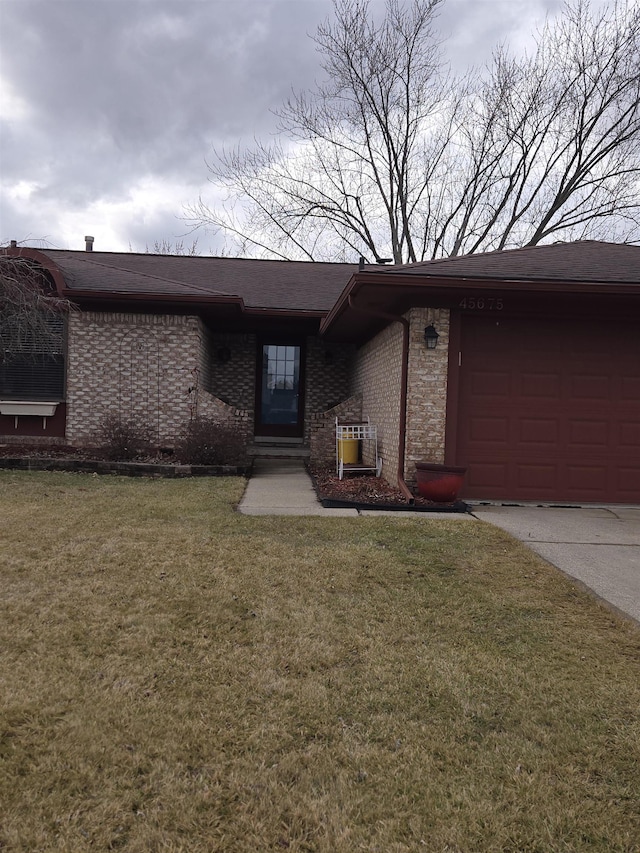 doorway to property with an attached garage, a shingled roof, a lawn, and brick siding