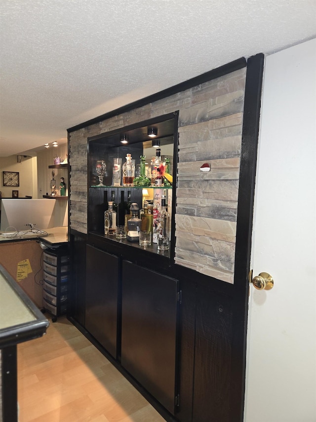 bar with a textured ceiling, a dry bar, and light wood-type flooring