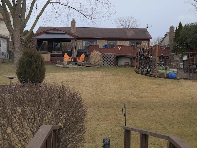 rear view of property with a deck, brick siding, fence, a gazebo, and a yard