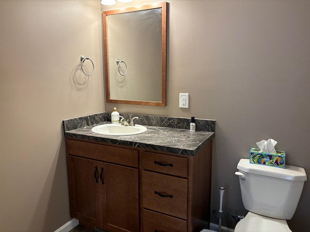 half bathroom with toilet, baseboards, and vanity