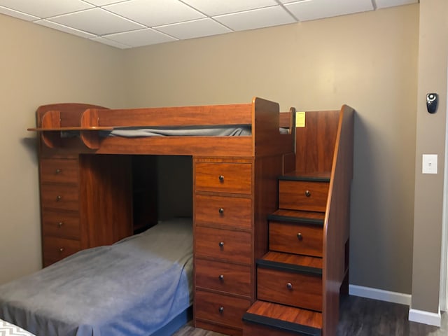 bedroom featuring a paneled ceiling, baseboards, and dark wood-type flooring