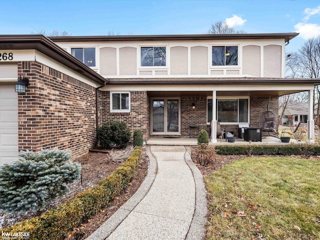 view of front of home featuring a garage, stucco siding, a patio area, and brick siding