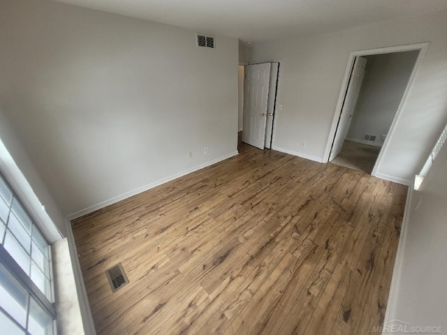 unfurnished bedroom featuring visible vents, ensuite bathroom, baseboards, and wood finished floors