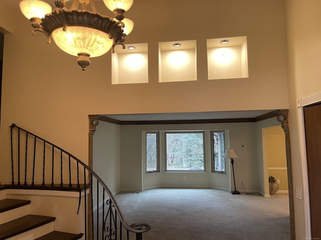 carpeted entrance foyer featuring a notable chandelier, a towering ceiling, baseboards, stairway, and crown molding