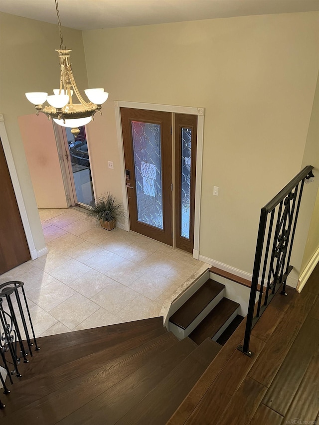 tiled foyer featuring stairs, baseboards, and a notable chandelier