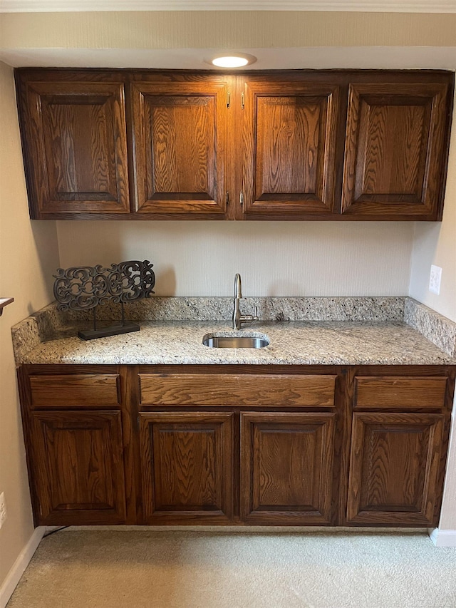 kitchen featuring light stone counters, baseboards, a sink, and dark brown cabinets