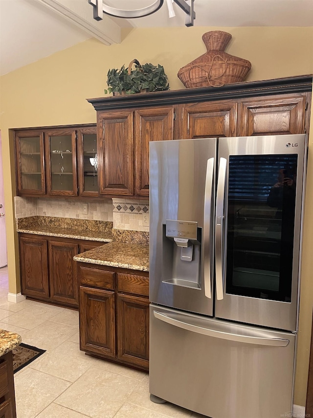 kitchen with light tile patterned floors, glass insert cabinets, vaulted ceiling, stainless steel refrigerator with ice dispenser, and backsplash