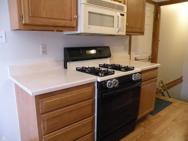 kitchen featuring range with gas cooktop, white microwave, light wood-style flooring, brown cabinets, and light countertops